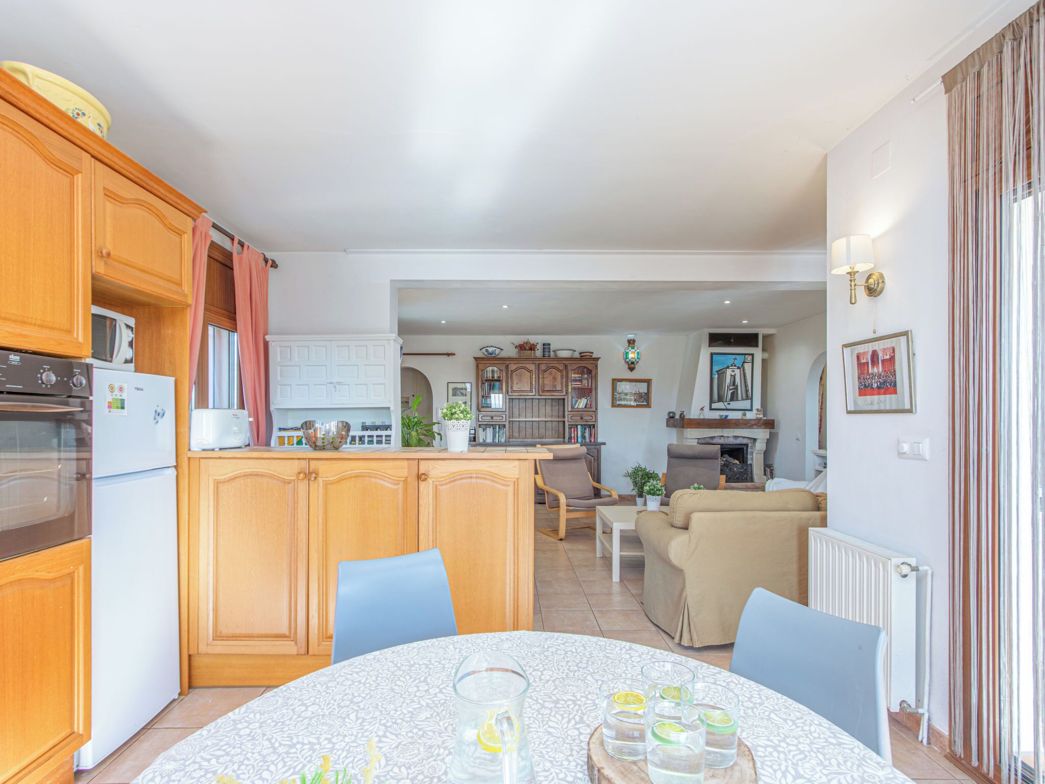 Een moderne keuken met houten kastjes, een eethoek met een ronde tafel, en een woonkamer met een bank.