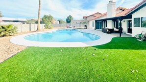 Une piscine entourée d’une pelouse et une maison avec un toit recouvert de tuiles rouges.