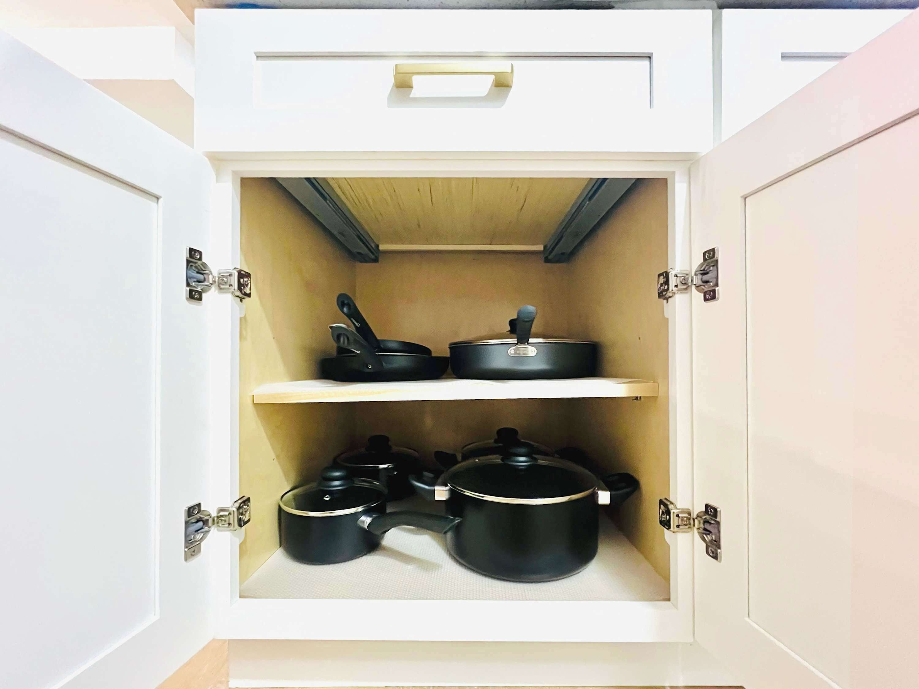 A kitchen cabinet with two shelves, each holding cookware.
