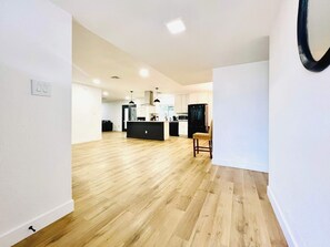 Eine geräumige Küche mit Holzboden, einem schwarzen Kühlschrank und einem Essbereich mit einem Stuhl.