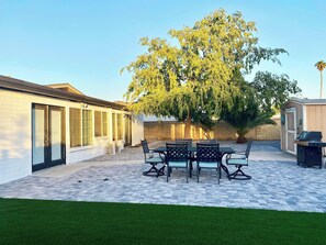 Eine Terrasse mit Tisch und Stühlen, ein Baum und eine Gartenhütte.