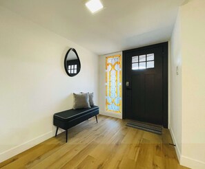 Ein Korridor mit einer Bank, einer Tür mit einem Glasfenster und einem Spiegel an der Wand.