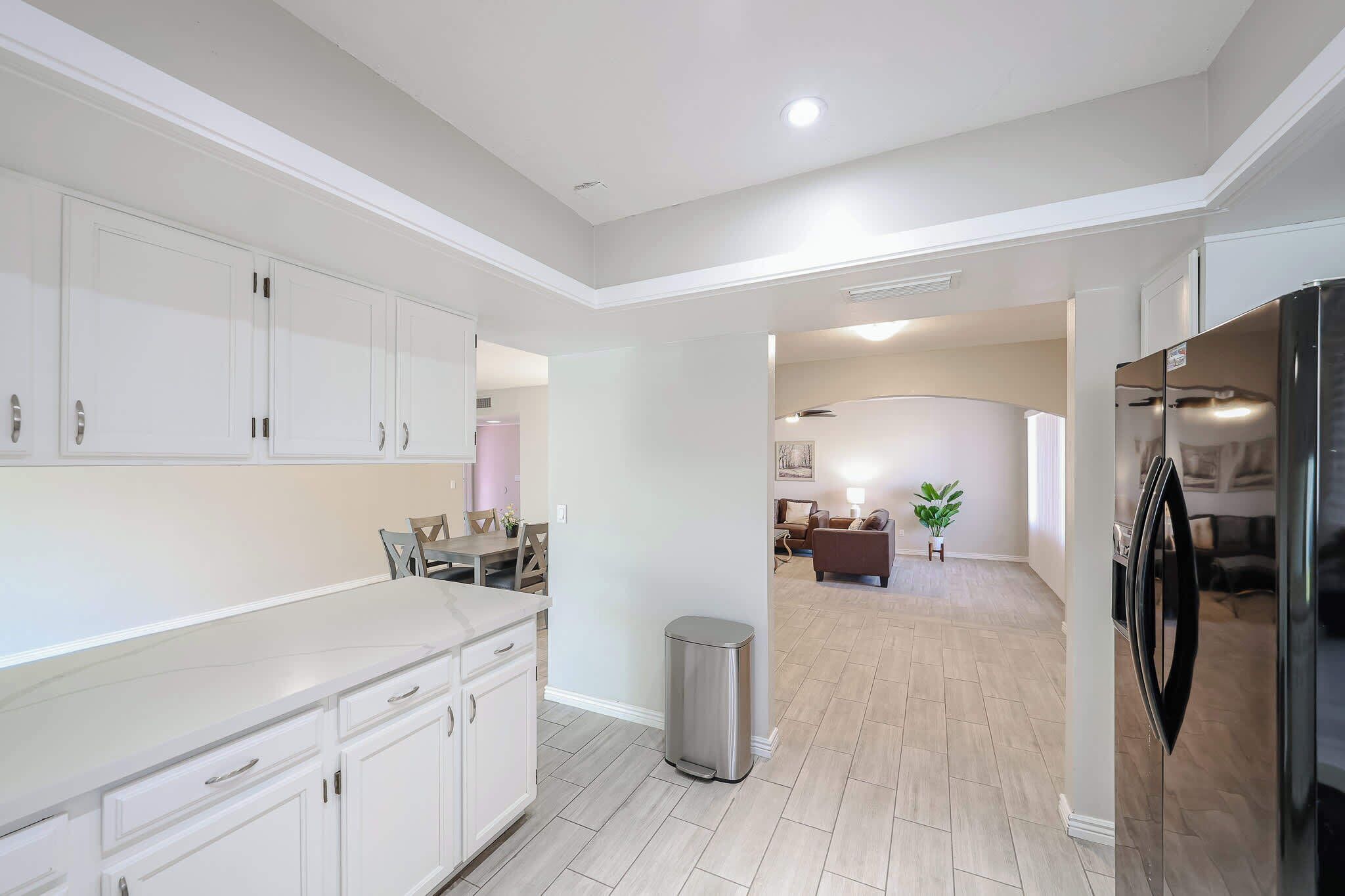 A modern kitchen with white cabinetry, a stainless steel refrigerator, and a trash can.