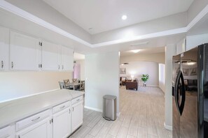 Una cocina moderna con muebles blancos, un refrigerador de acero inoxidable y un bote de basura.