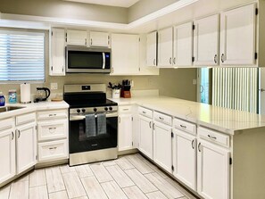 Una cocina moderna con armarios blancos, una estufa de acero inoxidable, un microondas y un horno empotrado.