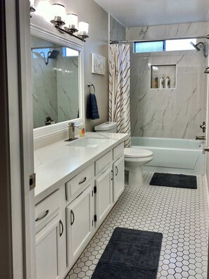 Un baño moderno con un espejo grande, un inodoro, una bañera y una ducha.