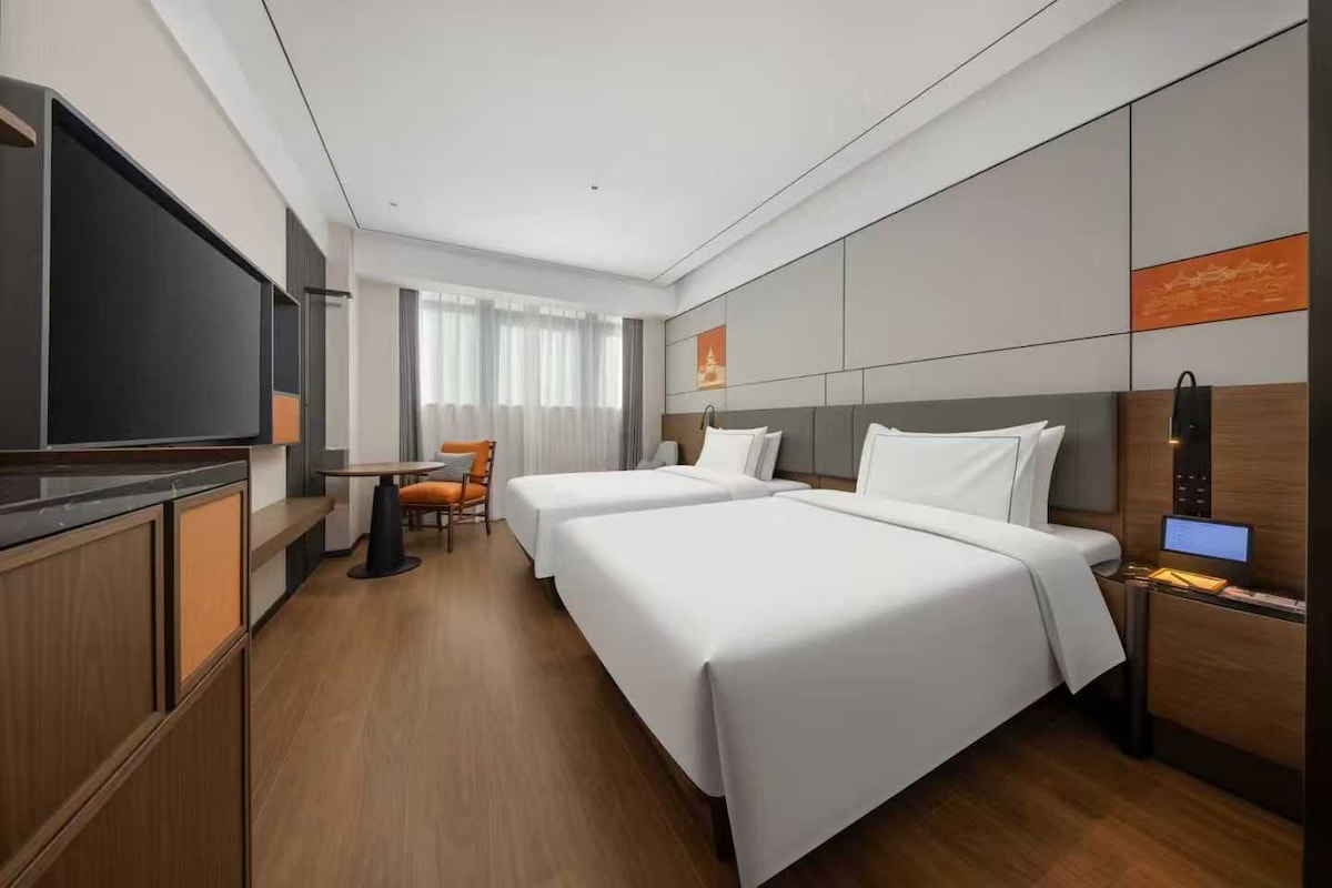 A hotel room with two beds, a TV, a desk, and a chair.