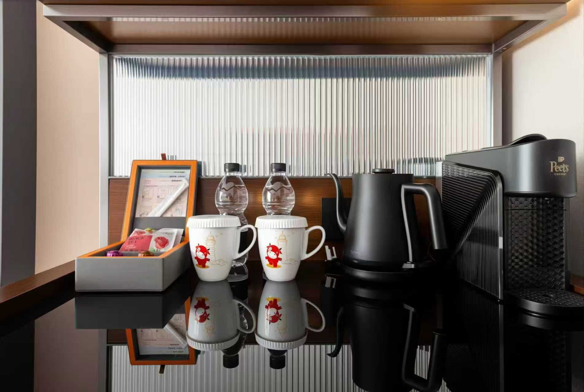 Ein Hotelzimmer mit einer Kaffeemaschine, zwei Tassen mit Zeichentrickfiguren, einer Wasserflasche und einem gerahmten Zertifikat auf dem Tisch.