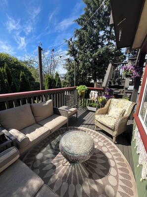 Eine Terrasse mit einer Couch, einem Sessel und einem runden Tisch, umgeben von Topfpflanzen und einer Treppe.