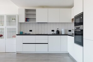 Eine moderne Küche mit weißen Schränken, einer Fischgrätmuster-Fliesenrückwand und einem eingebauten Backofen.