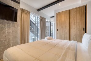 Ein modernes Schlafzimmer mit einem großen Bett, einem an einer strukturierten Wand montierten Fernseher und einem Holzschrank.