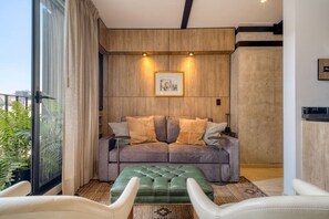 Ein modernes Wohnzimmer mit einer Couch, einem Hocker und zwei Sesseln, einem gerahmten Bild an der Wand und einem großen Fenster.