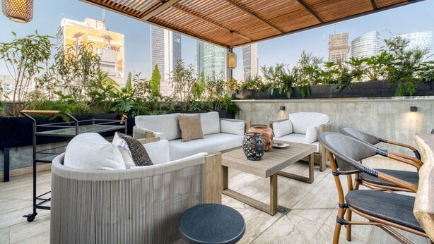 Ein Außenbereich mit Holz-Pergola, bequemen Sitzmöbeln und Blick auf die Skyline der Stadt.