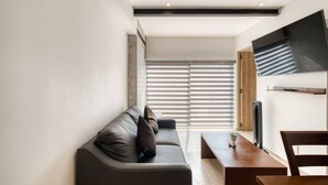 Ein modernes Wohnzimmer mit einer Couch, einem Esstisch und einem an der Wand befestigten Fernseher.