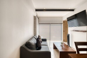 A modern living room with a sofa, a dining table, and a TV mounted on the wall. - Myla - 1BR - Roma Norte - Piso Bajo (Mexico City)