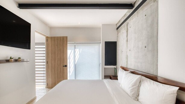 Ein modernes Hotelzimmer mit einem großen Bett, einem Holzkopfende, einem flachbildfernseher an der Wand und einem großen Fenster mit Jalousien.