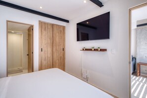 Ein Schlafzimmer mit einem Bett, einem an der Wand montierten Fernseher, einem Holzschrank und einem kleinen Regal mit Pflanzen.