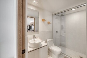 Ein modernes Badezimmer mit Duschkabine aus Glas, einem Waschbecken mit Spiegel und einer Toilette.