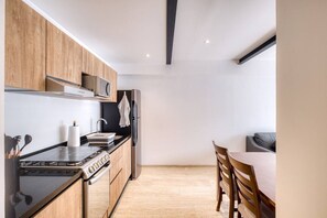 A modern kitchen with wooden cabinets, a gas stove, a microwave, and a refrigerator. - Myla - 1BR - Roma Norte - Piso Bajo (Mexico City)