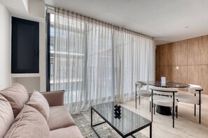 A modern living room with a sofa, a glass coffee table, a dining table with chairs, and sheer curtains. - Myla 05C - 2BR in Roma Norte - LowF (Mexico City)