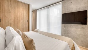 A modern hotel room with a large bed, wooden panel wall, large windows, and a built-in TV. - Myla 05C - 2BR in Roma Norte - LowF (Mexico City)