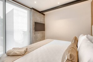 Ein modernes Hotelzimmer mit einem großen Bett, einem an der Wand montierten Flachbildfernseher und einem großen Fenster mit Blick nach außen.