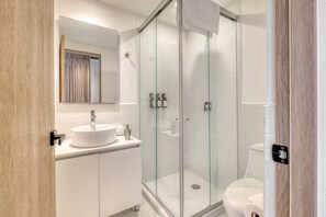 Ein modernes Badezimmer mit einer begehbaren Glasdusche, einem weißen Waschbecken und einer Toilette.