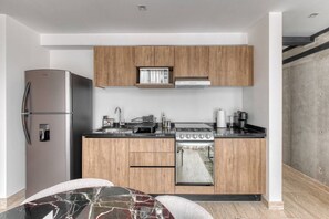 Eine moderne Küche mit Holzschränken, einem Edelstahlkühlschrank, einem eingebauten Ofen und einem Esstisch aus Marmor.