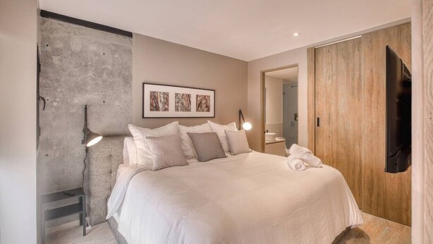 Ein modernes Schlafzimmer mit einem großen Bett, einem Holzschrank, einem Flachbildfernseher und einem gerahmten Kunstwerk an der Wand.