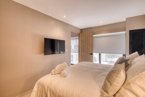Ein Schlafzimmer mit einem großen Bett, einem flachbildfernseher an der Wand und einem Fenster mit Blick nach draußen.