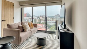 Ein modernes Wohnzimmer mit Sofa, Couchtisch und Fernseher, große Fenster mit Blick auf die Stadt.