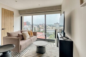 A modern living room with a sofa, coffee table, and TV, large windows with a city view. - Myla 904C - 1BR In Roma Norte - HighF (Mexico City)
