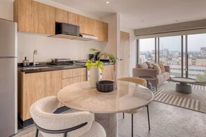 A modern kitchen with wooden cabinets, a microwave, and a dining area with a round table and chairs. - Myla 904C - 1BR In Roma Norte - HighF (Mexico City)