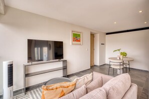 A modern living room with a flat-screen TV, a sofa, a small round table, and a potted plant. - Myla 904C - 1BR In Roma Norte - HighF (Mexico City)