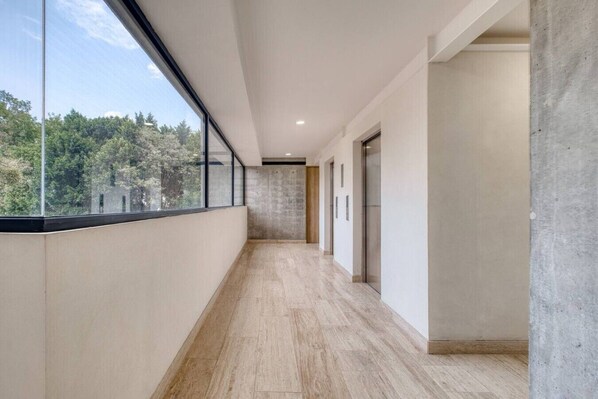A corridor with a large window, a concrete wall, and a door. - Myla 904C - 1BR In Roma Norte - HighF (Mexico City)