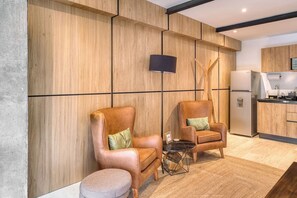 Eine moderne Küche mit Holzvertäfelung, zwei Ledersesseln, einem kleinen Beistelltisch und einem Kühlschrank.
