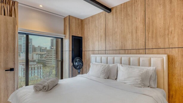 Une chambre moderne avec un grand lit, un ventilateur et une vue sur la ville grâce à une grande fenêtre.