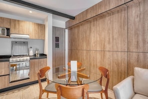 A modern kitchen with a gas stove, oven, and microwave, a glass dining table with four chairs, and a white sofa. - Casa Myla - 1BR in Roma Norte - HighF (Mexico City)