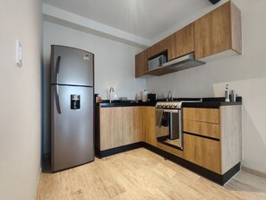 Eine moderne Küche mit Edelstahlkühlschrank, Holzausbau, Backofen und schwarzem Arbeitsplatz.