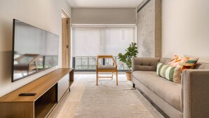 Ein modernes Wohnzimmer mit einem Flachbildfernseher, einer hölzernen Bank, einer Couch mit Kissen und einer Topfpflanze.