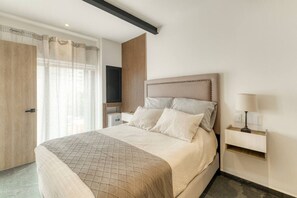 A bedroom with a bed, a bedside table with a lamp, a TV, and a wooden door. - Myla-02C- 1BR Roma Norte - LowF (Mexico City)