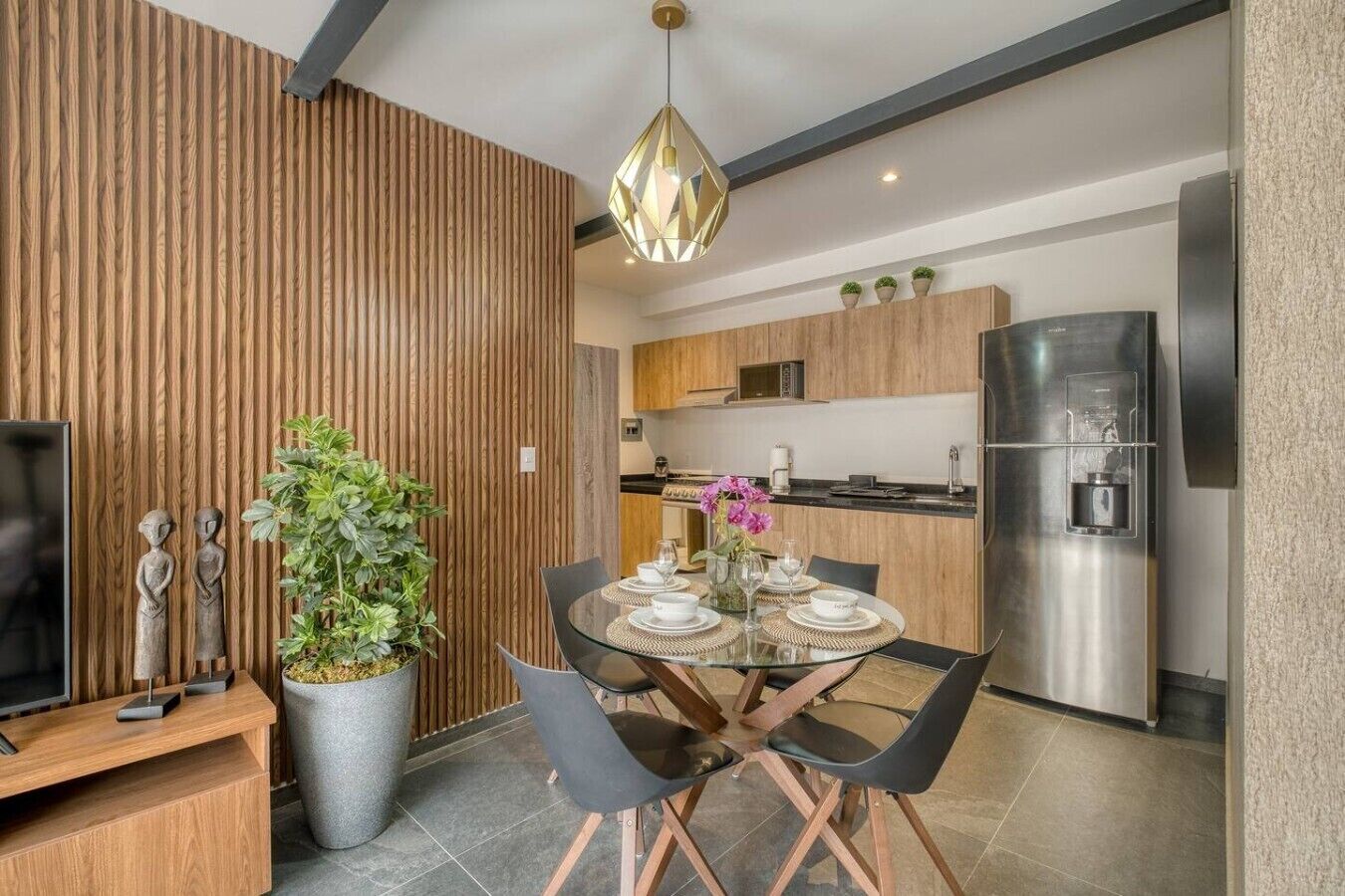 A modern kitchen with stainless steel appliances, a dining area with a glass table, and a large potted plant.