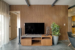 A modern living room with a large flat-screen TV, wooden panel wall, and a potted plant. - Myla-02C- 1BR Roma Norte - LowF (Mexico City)