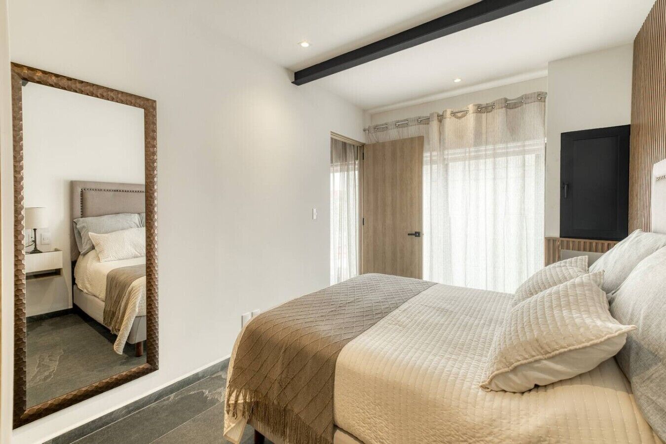 A bedroom with a large bed, a mirror, a wardrobe, and a television.