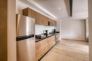 A modern kitchen with wooden cabinets, a stainless steel refrigerator, and a black countertop. - Myla - Casa Calderon - Roma Norte (HF) (Mexico City)