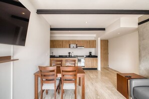 A modern kitchen with wooden cabinets, a dining area with two wooden chairs, and a TV mounted on the wall. - Myla - Casa Calderon - Roma Norte (HF) (Mexico City)