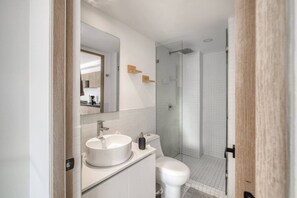 A modern bathroom with a white sink, toilet, and glass-enclosed shower. - Myla - Casa Calderon - Roma Norte (HF) (Mexico City)