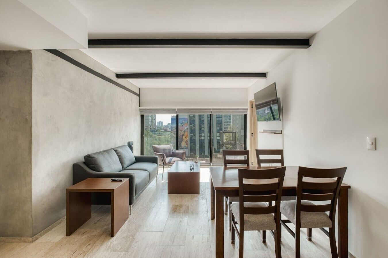 A modern living room with a sofa, coffee table, dining table, chairs, and a TV mounted on the wall.