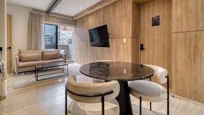 Ein modernes Wohnzimmer mit einer Couch, einem runden Tisch mit Stühlen, einem flachbildfernseher an der Wand und einem großen Fenster mit Vorhängen.