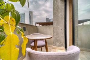 Un balcón con una mesa redonda y dos sillas, un muro de concreto y vistas de edificios de la ciudad.